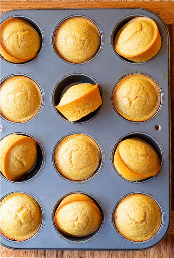 Top down view muffin tin with a dozen baked corn bread muffins.