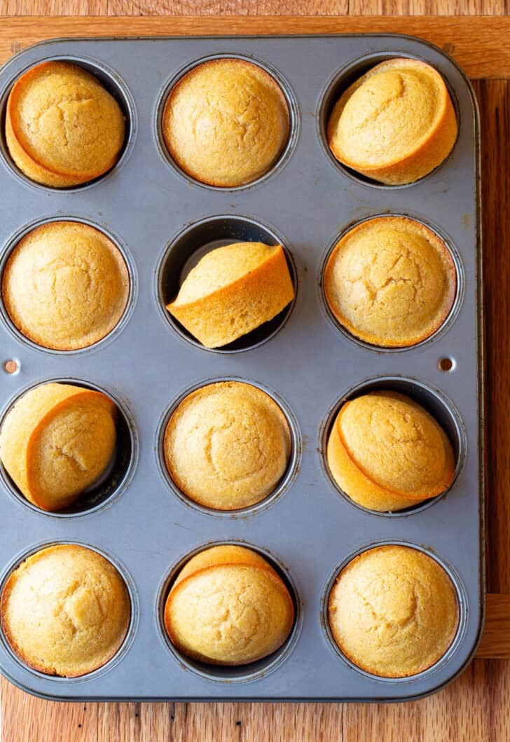 Top down view muffin tin with a dozen baked corn bread muffins.