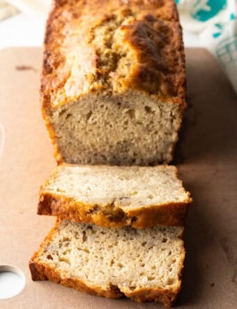 Loaf of banana bread on a cutting board, with two slices showing to camera.