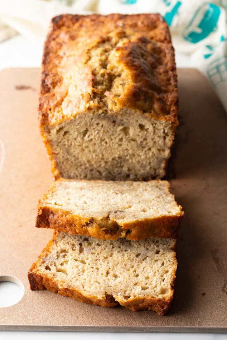 Loaf of banana bread on a cutting board, with two slices showing to camera.