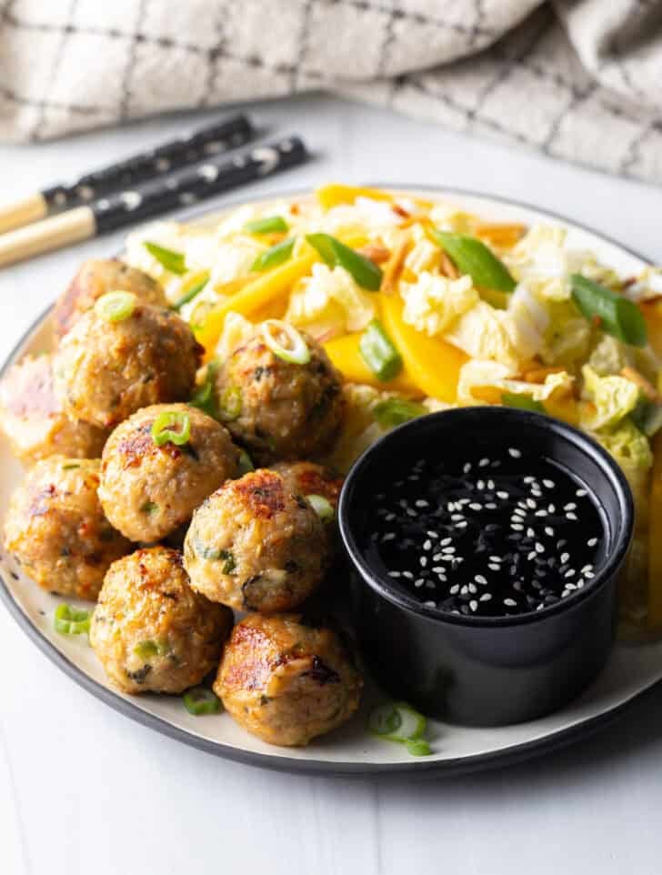 Plate covered half Thai turkey meatballs and half chopped Asian salad, plus a black ramekin of dipping sauce.