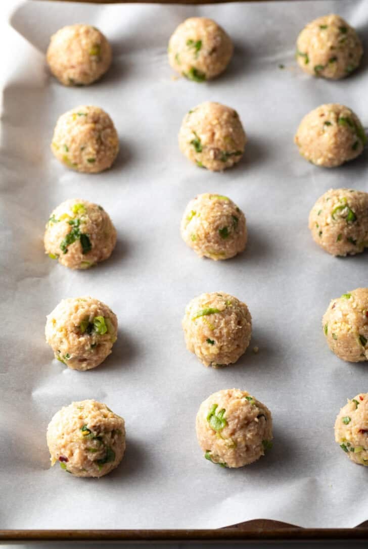 15 raw turkey meatballs on a baking sheet.
