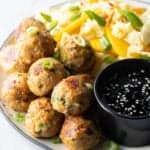 Plate covered half Thai turkey meatballs and half chopped Asian salad, plus a black ramekin of dipping sauce.