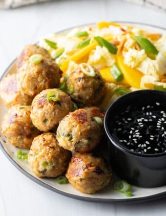 Plate covered half Thai turkey meatballs and half chopped Asian salad, plus a black ramekin of dipping sauce.