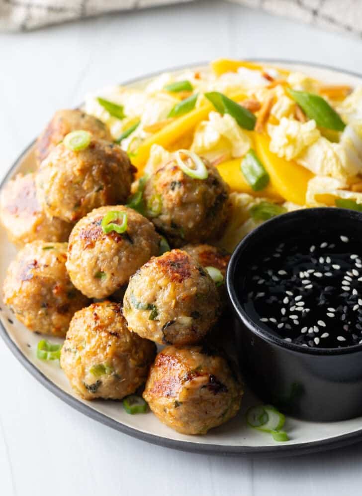 Plate covered half Thai turkey meatballs and half chopped Asian salad, plus a black ramekin of dipping sauce.