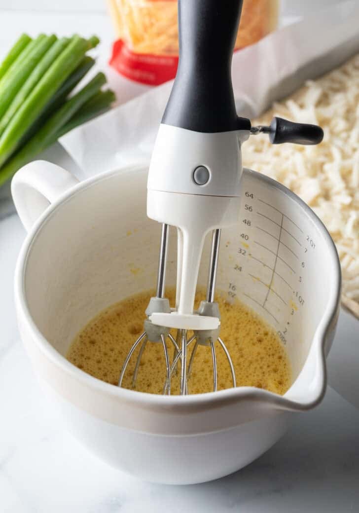 White mixing pitcher with egg mixture and a hand mixer.