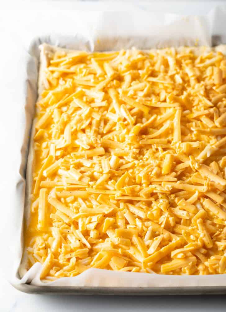 Shredded cheddar cheese on the top of an unbaked rectangle pizza.