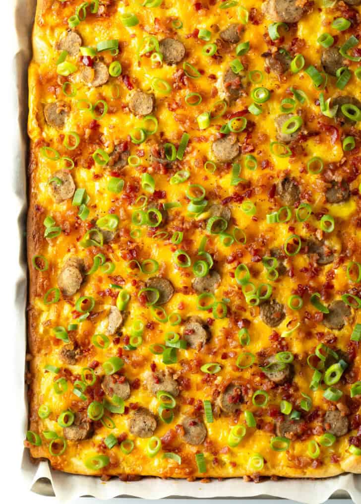 Rectangle baking sheet tray with breakfast pizza, loaded with cheese, sausage, and green onions.