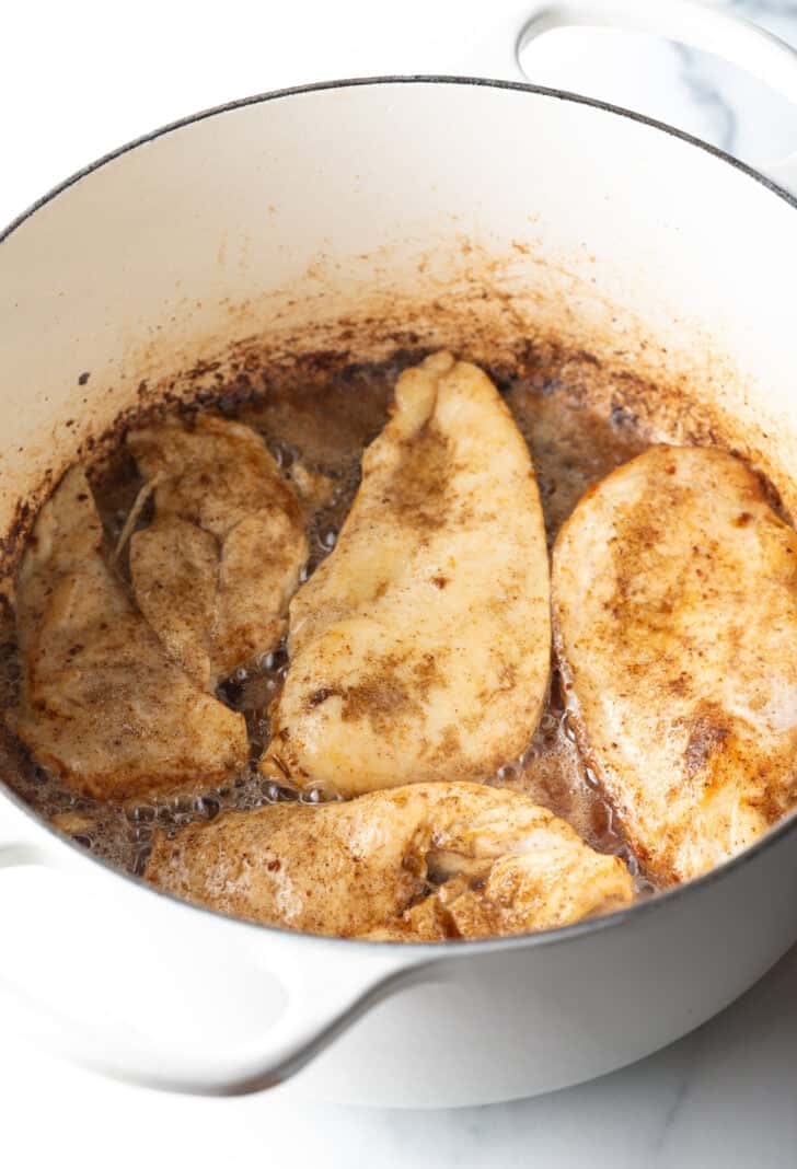 4 chicken breasts cooking in a deep white pot.