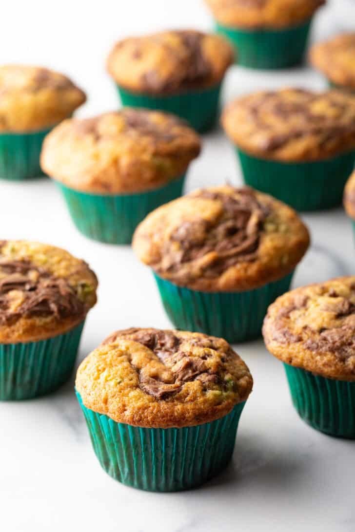 A dozen zucchini muffins with Nutella swirls, in green cupcake wrappers.