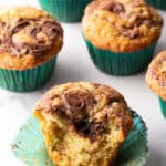 A dozen zucchini muffins with Nutella swirls, in green cupcake wrappers. One muffin has been split in half to show the inside.
