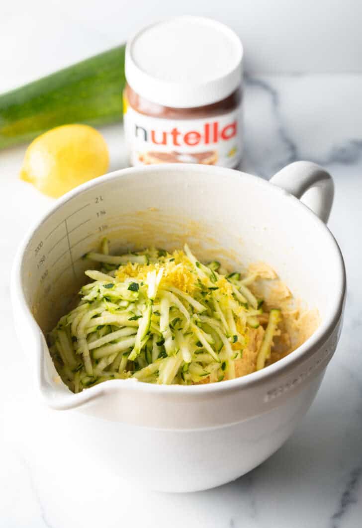 White measuring bowl with shredded zucchini and lemon zest.