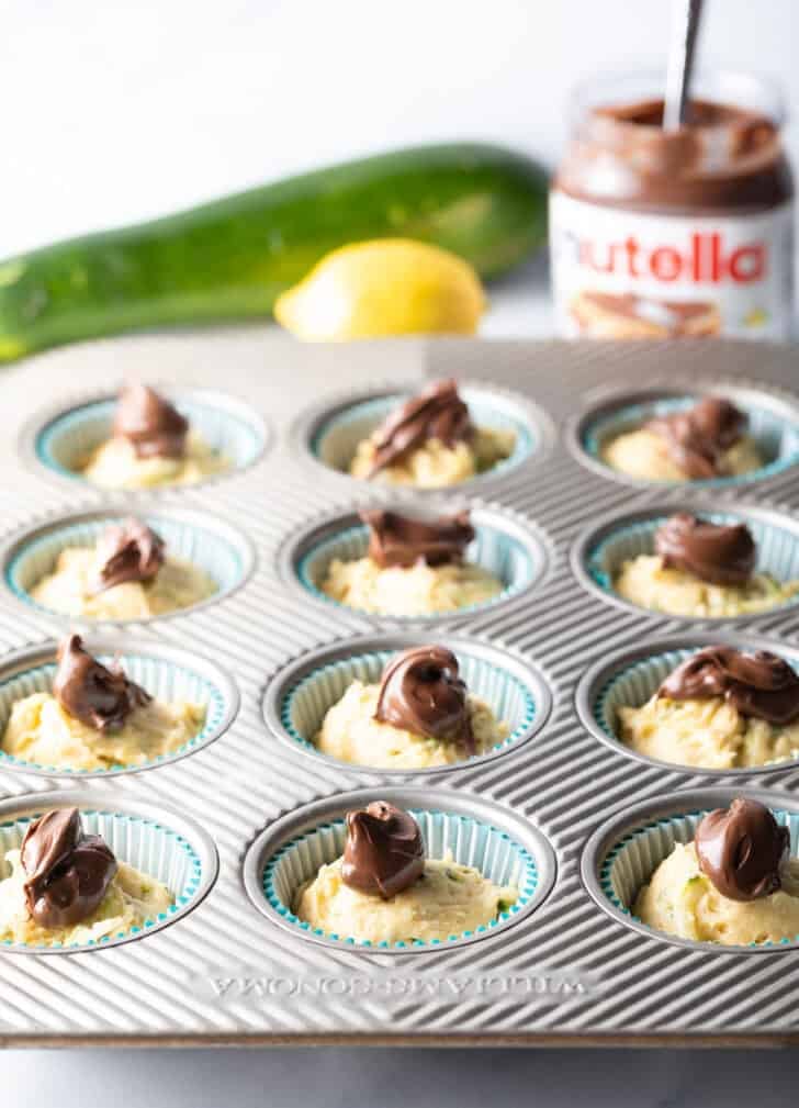 Raw muffin batter in a cupcake tin, with a dollop of nutella on top of each.