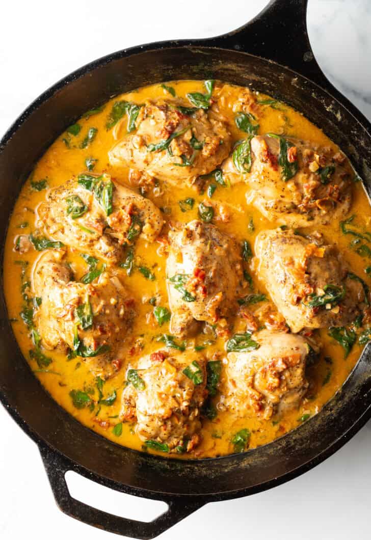 Top down view cast iron skillet packed with chicken thighs in a creamy Tuscan cream sauce.