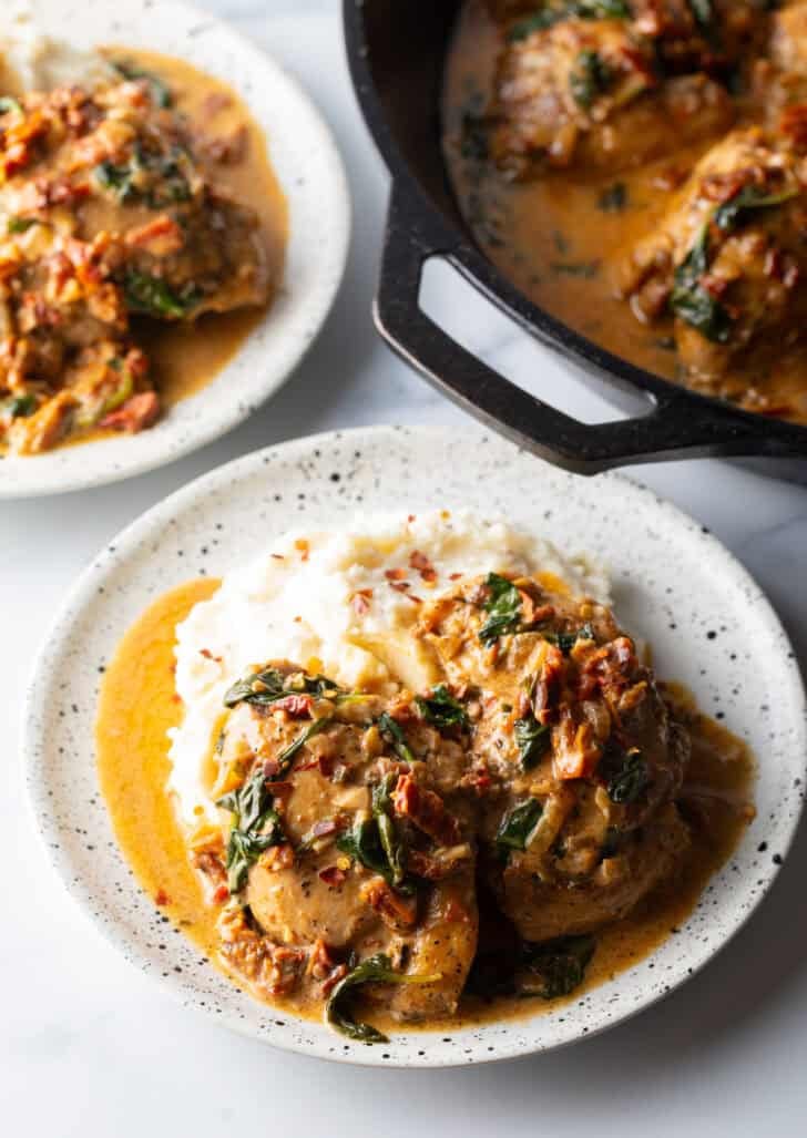 Two pieces of Tuscan chicken on a plate with mashed potatoes and creamy gravy.