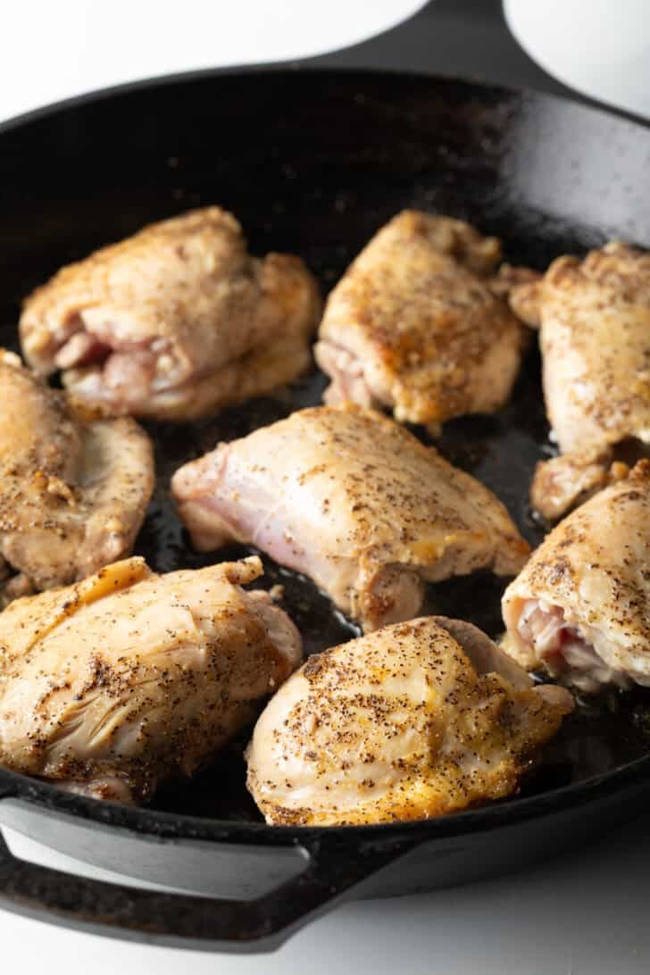 8 chicken thighs cooking in a large cast iron skillet.