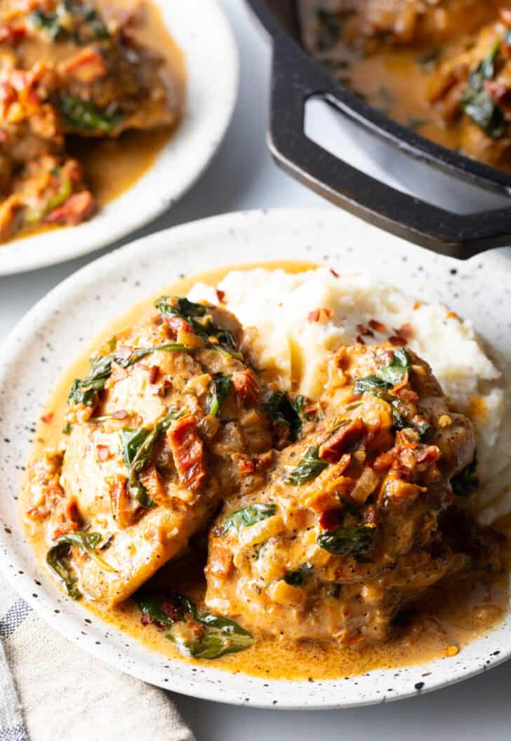 Two pieces of Tuscan chicken on a plate with mashed potatoes and creamy gravy.