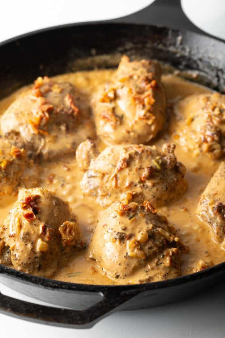 Cooked chicken thighs in cream sauce in a cast iron skillet.
