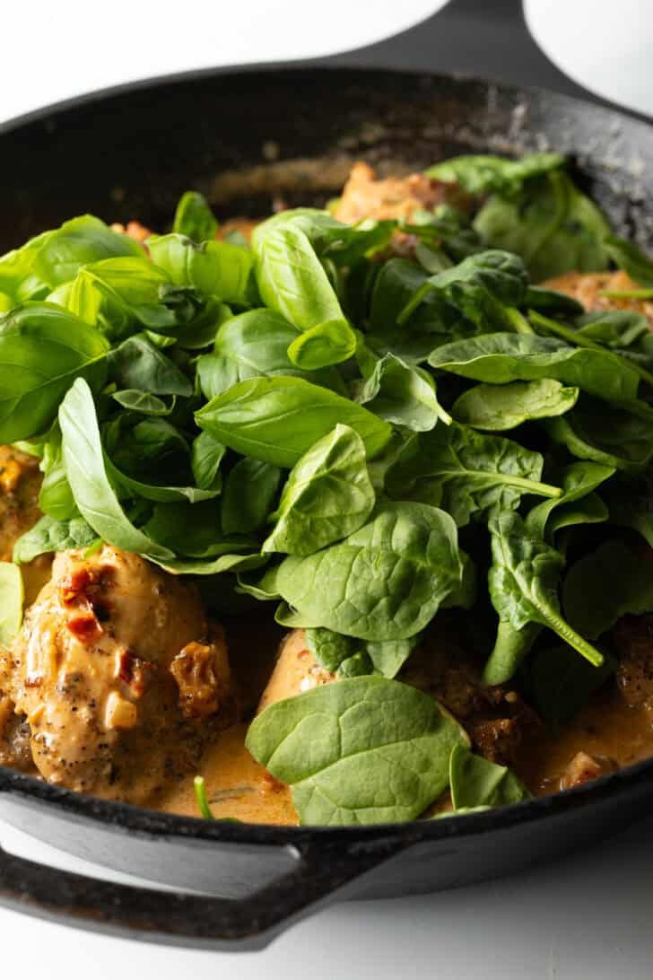 Adding fresh baby spinach leaves on top of the skillet with chicken thighs and cream sauce.