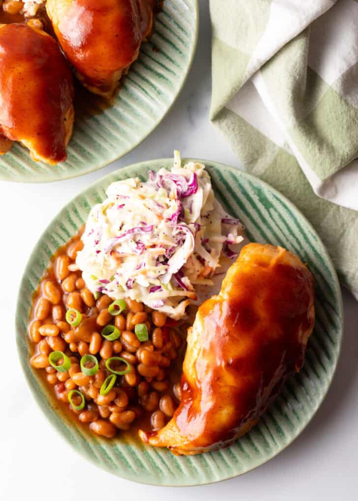 Top down view green plate with bbq chicken, coleslaw, and baked beans.