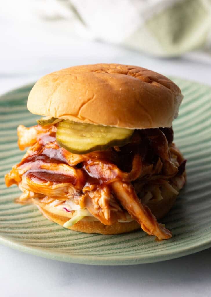 Crockpot bbq chicken sandwich on a hamburger bun, loaded with coleslaw and pickles.