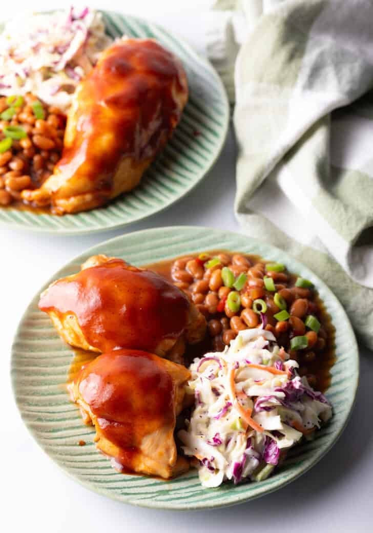 Green plate with bbq chicken, coleslaw, and baked beans.