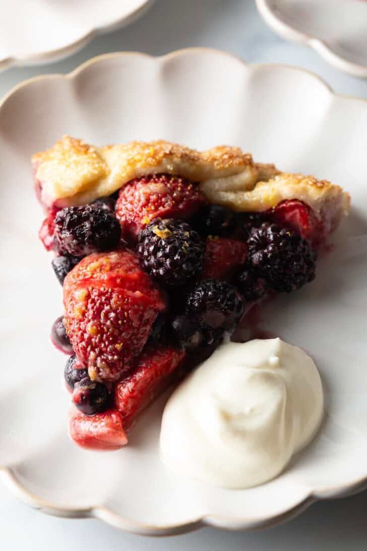 Slice of crostata filled with berries, one a white plate with a scoop of ricotta cream.