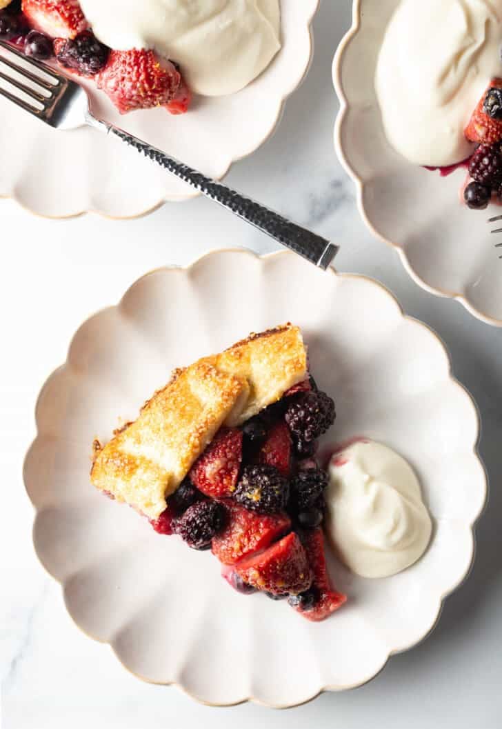 Slice of crostata filled with berries, one a white plate with a scoop of ricotta cream.