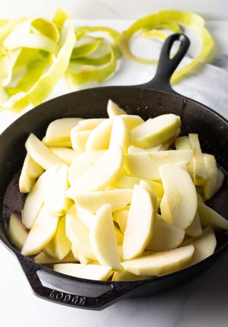 Mounded pile of raw apple slices in a cast iron skillet.