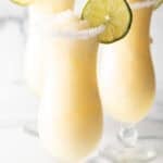 3 frozen margaritas in hurricane glasses, each garnished with a slice of lime and salt around the rim.