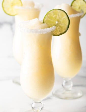 3 frozen margaritas in hurricane glasses, each garnished with a slice of lime and salt around the rim.
