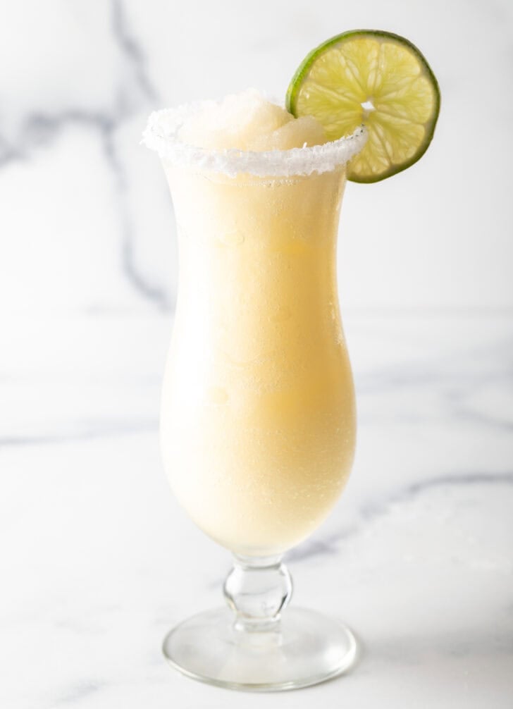 Frozen margarita in a hurricane glass, garnished with a slice of lime and salt around the rim.