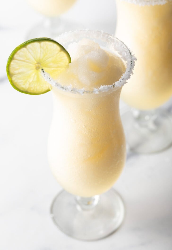 Frozen margarita in a hurricane glass, garnished with a slice of lime and salt around the rim.