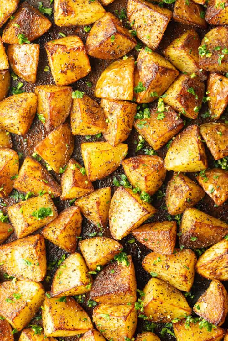 Top down view a rimmed baking sheet covered with chunks of crispy golden potatoes.