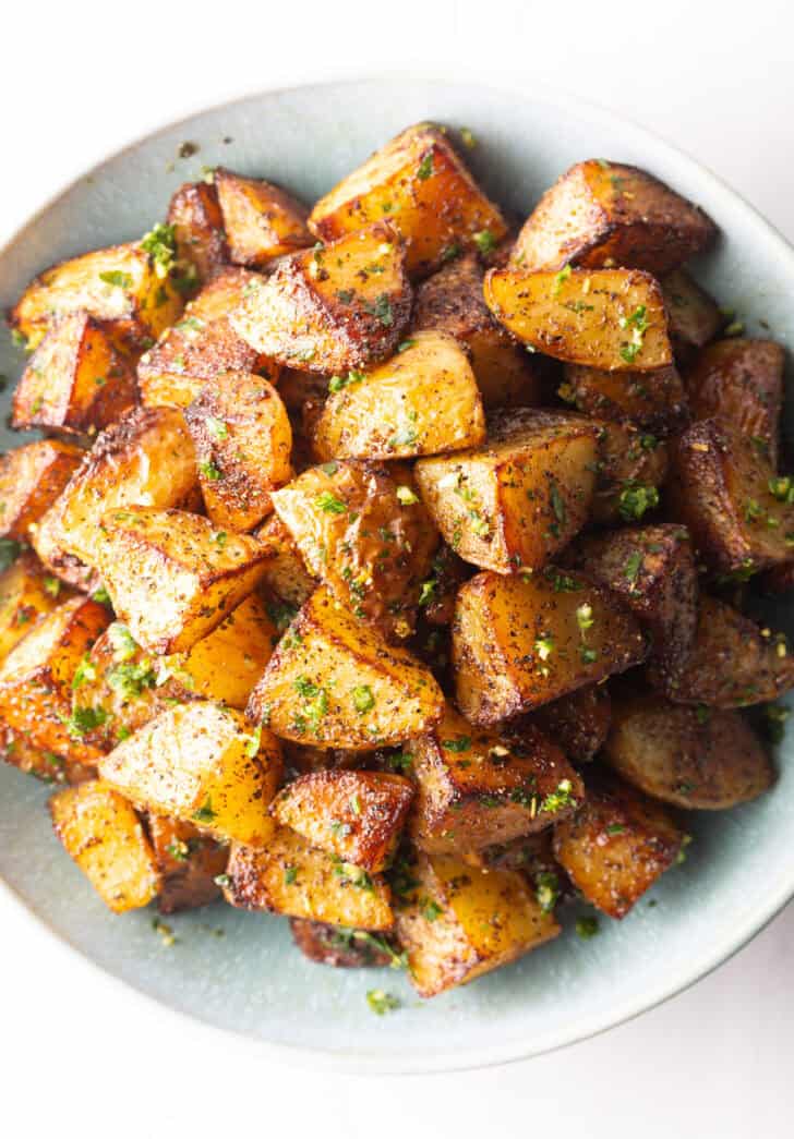 Top down view of a white bowl brimming with pieces of golden crispy Yukon potatoes.