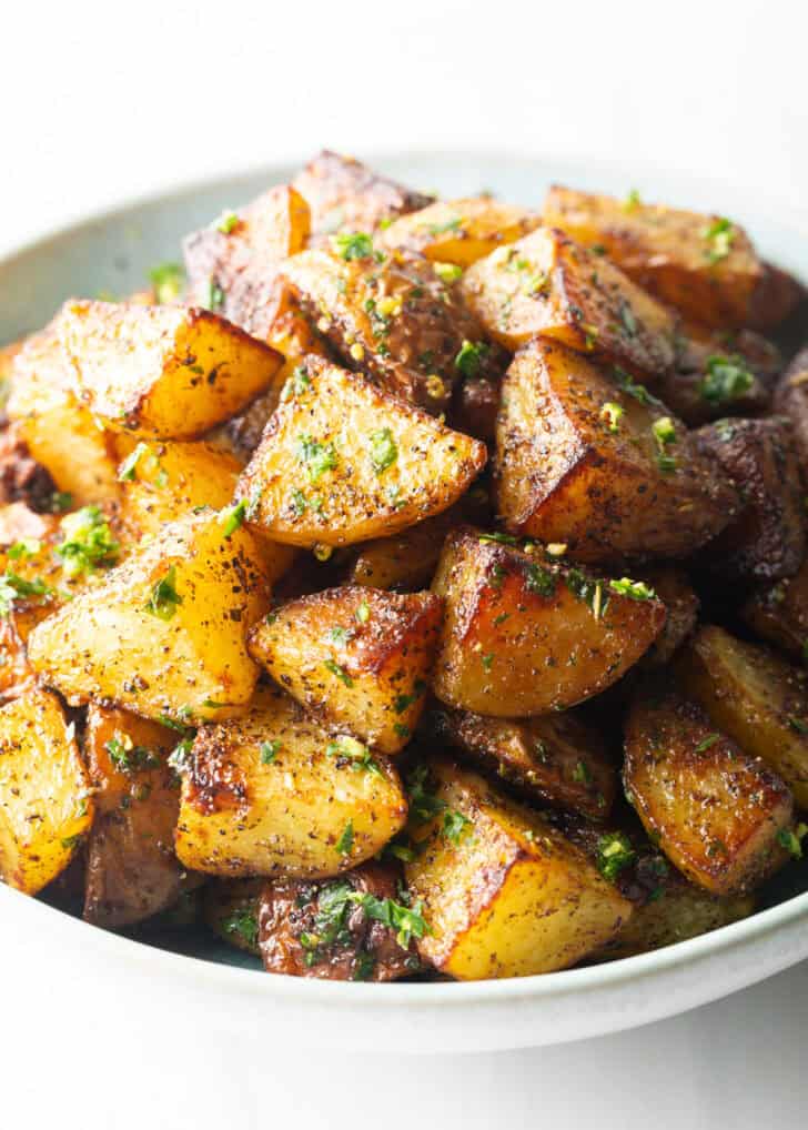 White bowl brimming with pieces of golden crispy Yukon potatoes.