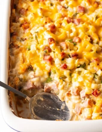 Top down view white casserole dish with ham and potatoes, and a spoon in the dish where a serving has been removed.