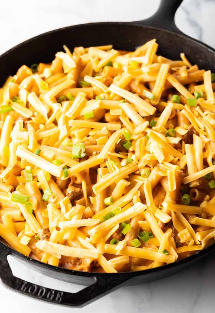 Adding shredded cheddar cheese on top of the noodle and beef casserole.