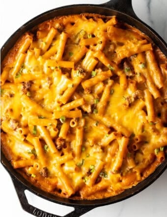 Top deep black cast iron skillet with long noodles, ground beef, and cheese.