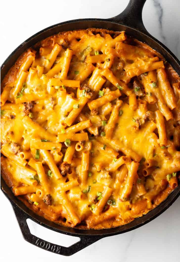 Top deep black cast iron skillet with long noodles, ground beef, and cheese.