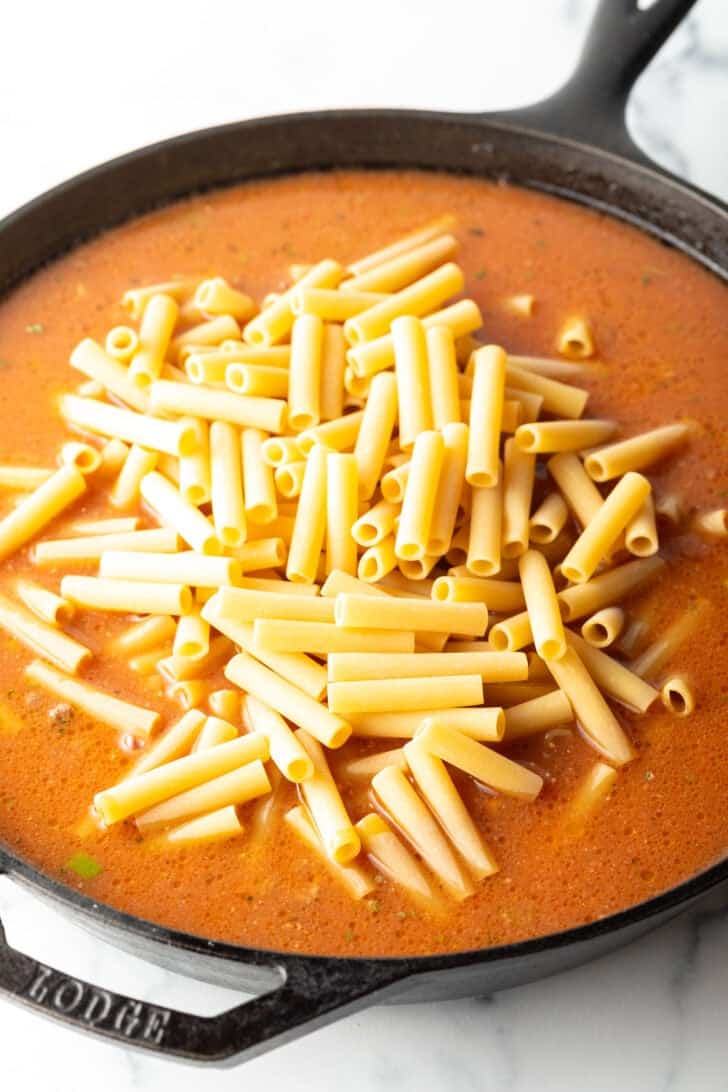 Adding long pasta noodles to a skillet with ground beef and tomato sauce.