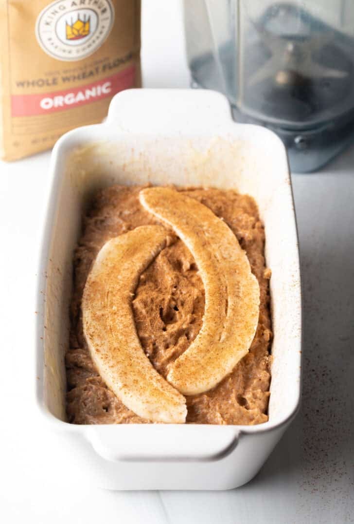 Batter in a white loaf pan, topped with two pieces of a banana sliced in half.