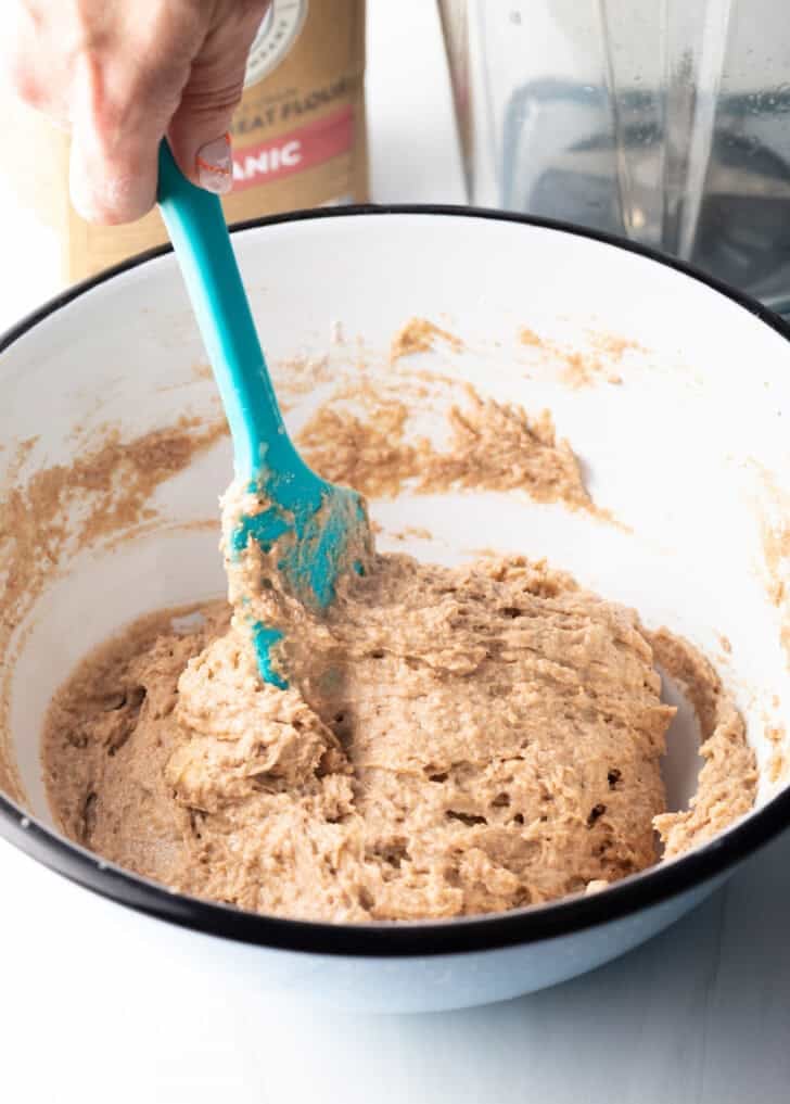 Stirring the batter with a blue spatula in a white mixing bowl.