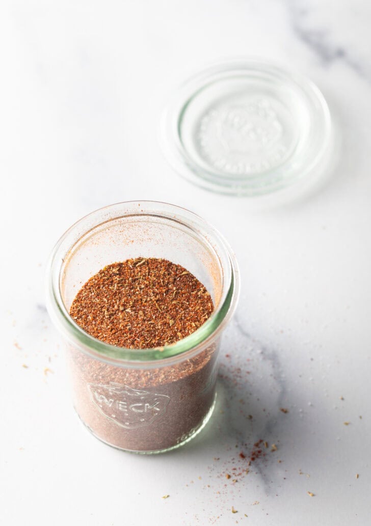 Tall glass jar filled with taco seasoning blend.