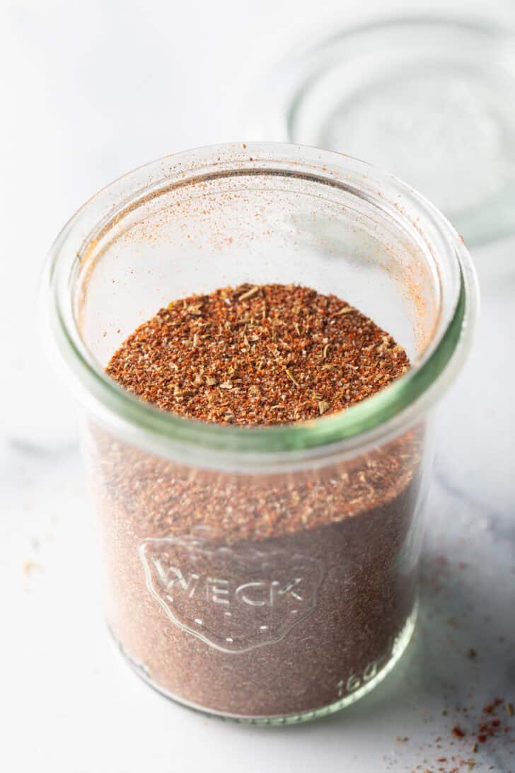 Tall glass jar filled with taco seasoning blend.