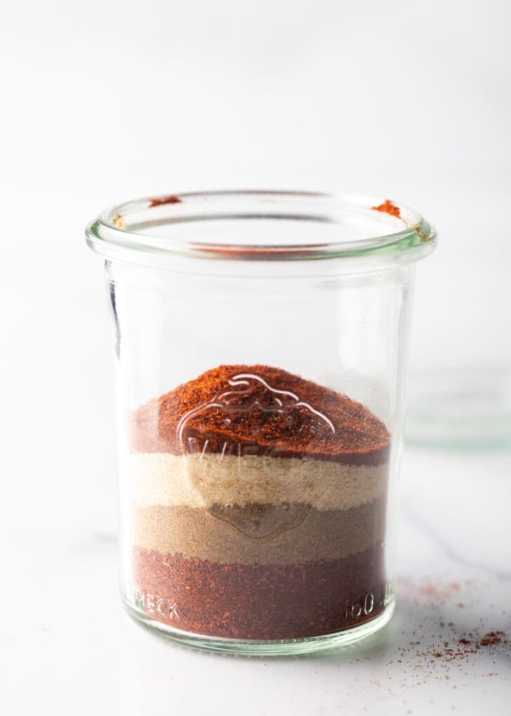Layers of different seasonings in a tall glass jar.