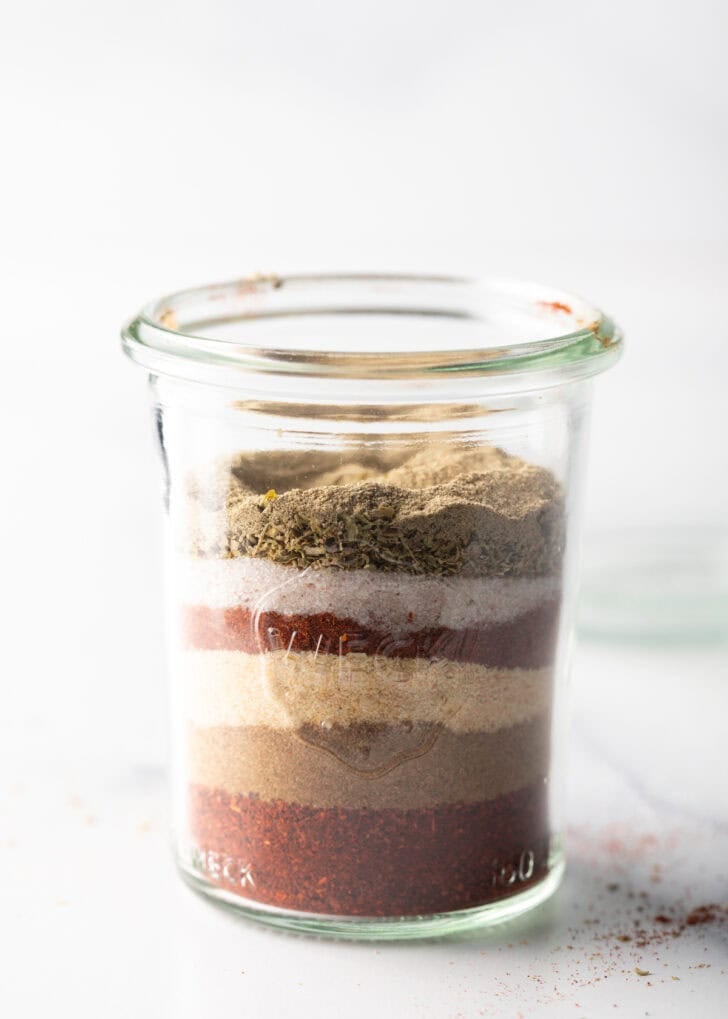 Layers of different seasonings in a tall glass jar.