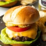 Aair fryer hamburger loaded with cheese, lettuce, tomatoes and pickle slices on a plate.