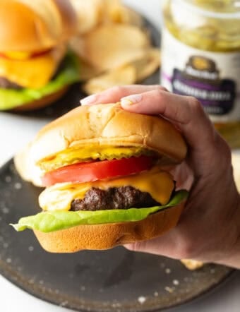 Hand holding a juicy air fryer hamburger loaded with cheese, lettuce, tomatoes and pickle slices.