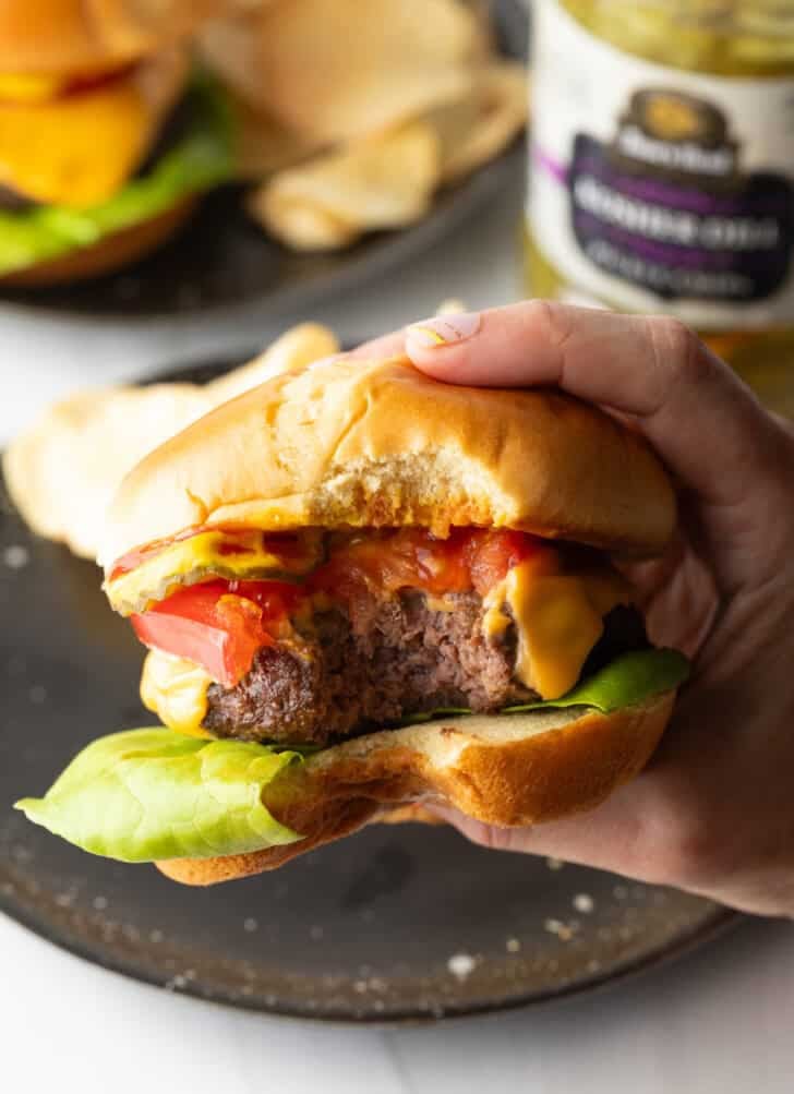 Hand holding a hamburger to camera, with bite taken out.